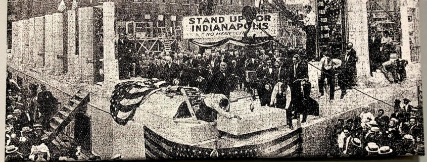 Indy Star black and white photo of a crowd gathered around mayor laying a cornerstone at a construction site with a banner overhead reading Stand Up for Indianapolis No Mean City
