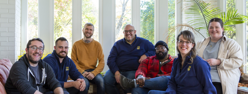 1909 team sitting on couches in front of a window at the Peace Learning Center